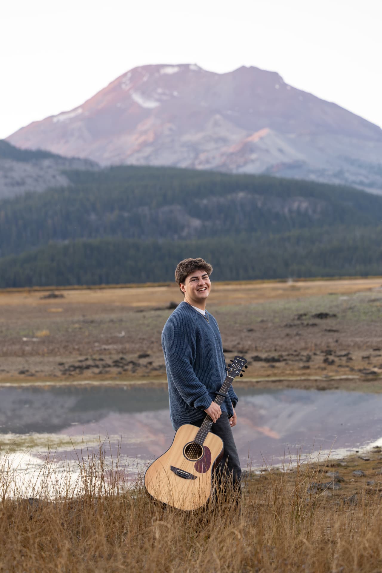 Senior guy holding a guitar with a Cascade peak behind him