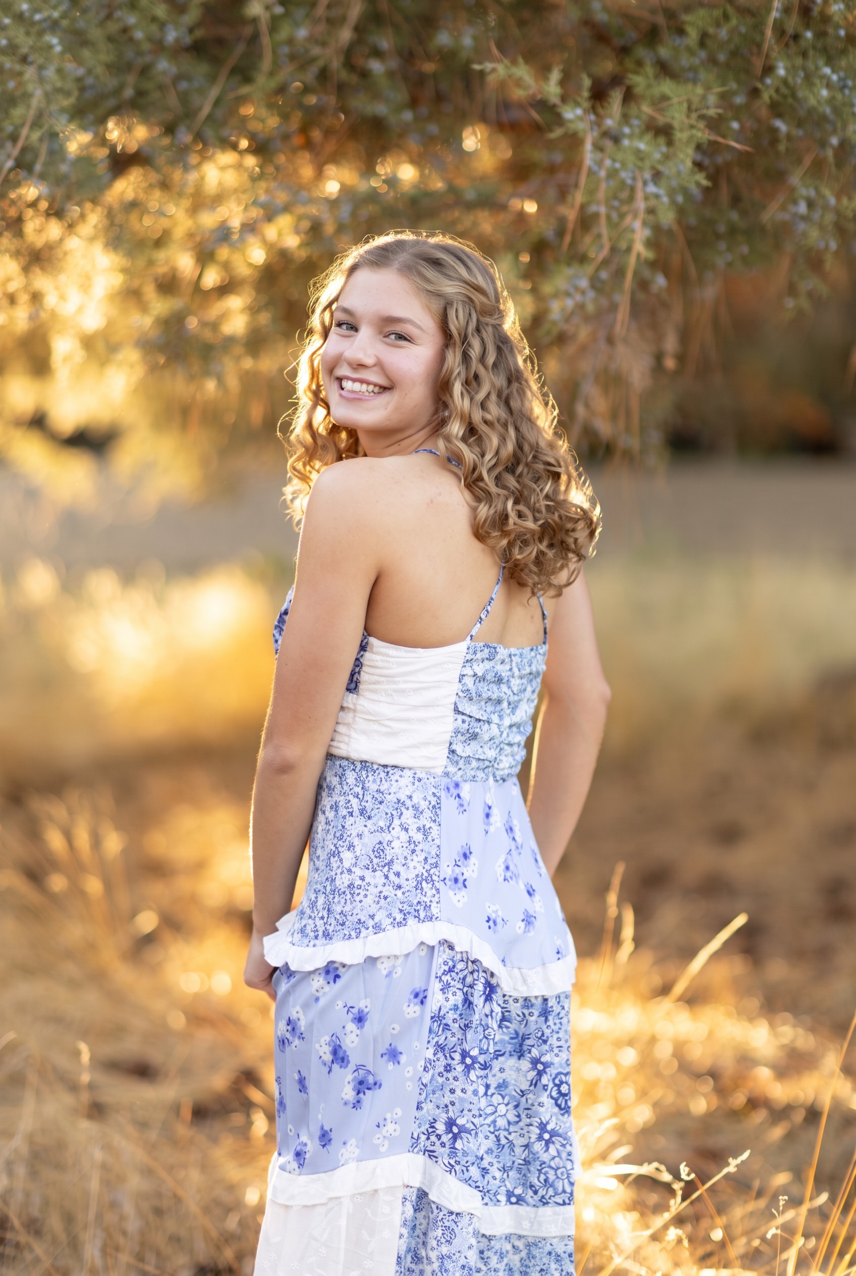 Senior girl turning toward the camera in a blue floral dress beneath golden autumn trees
