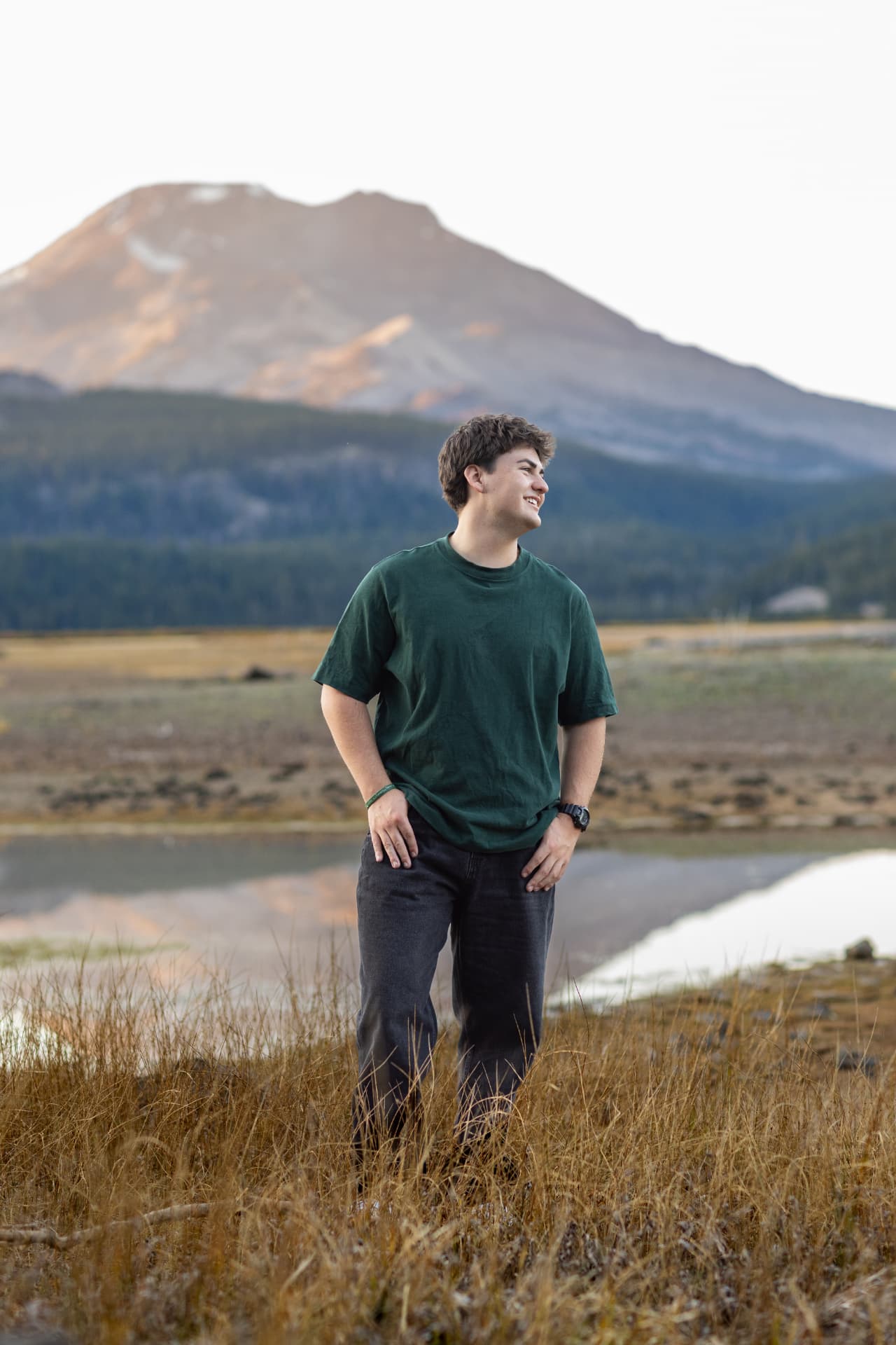 Senior guy laughing in golden grass with a sunlit Cascade peak behind him